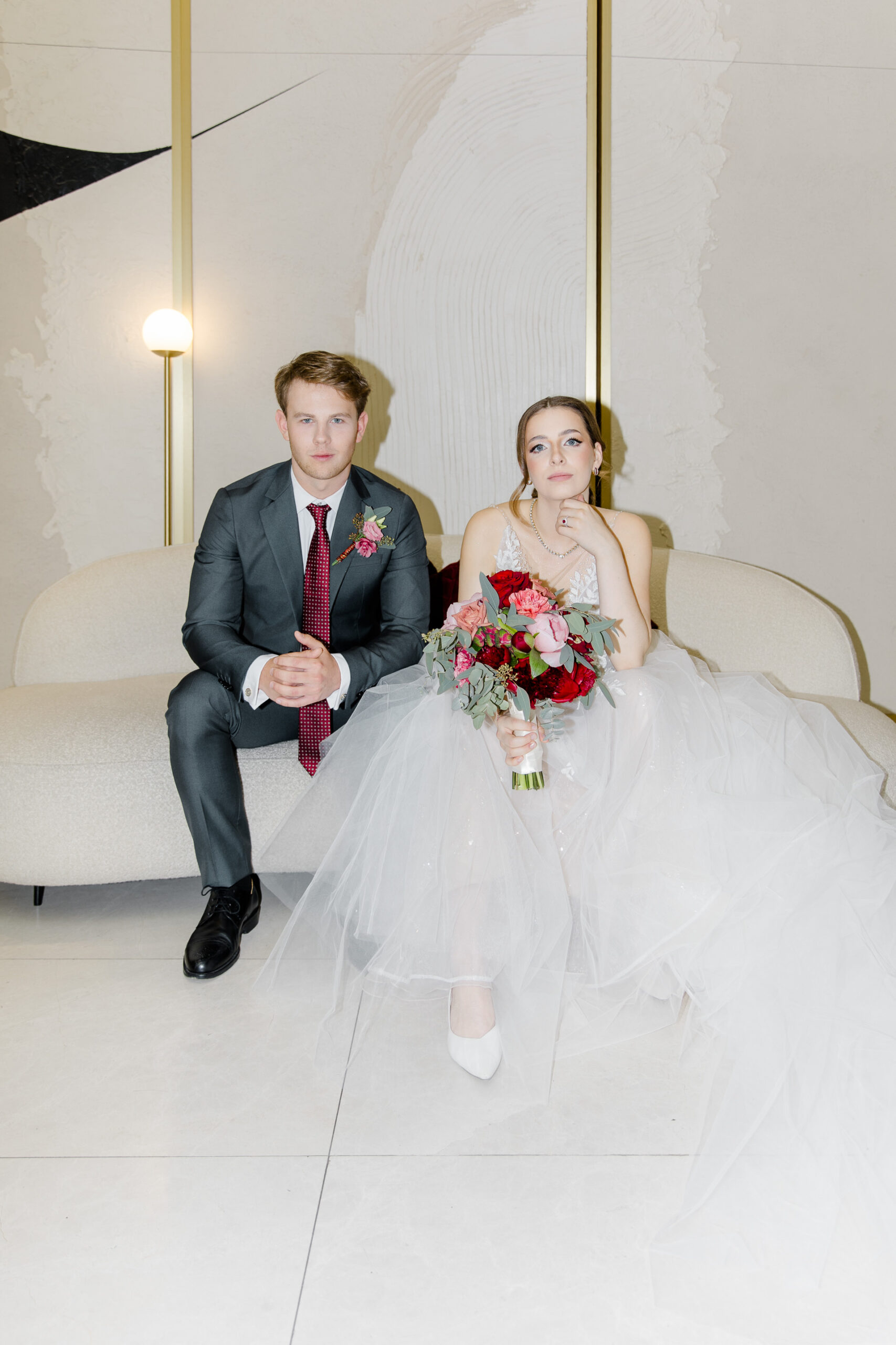 Hochzeitsfotograf Wien: Ein direkt in die Kamera schauendes Brautpaar sitzt nebeneinander auf einem hellen Sofa im Palais Almanac.