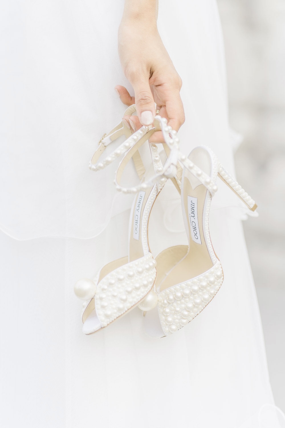 Hochzeitsfotograf Wien: Eine Frauenhand hält luxuriöse Hochzeitsschuhe vor einem hellen HIntergrund.