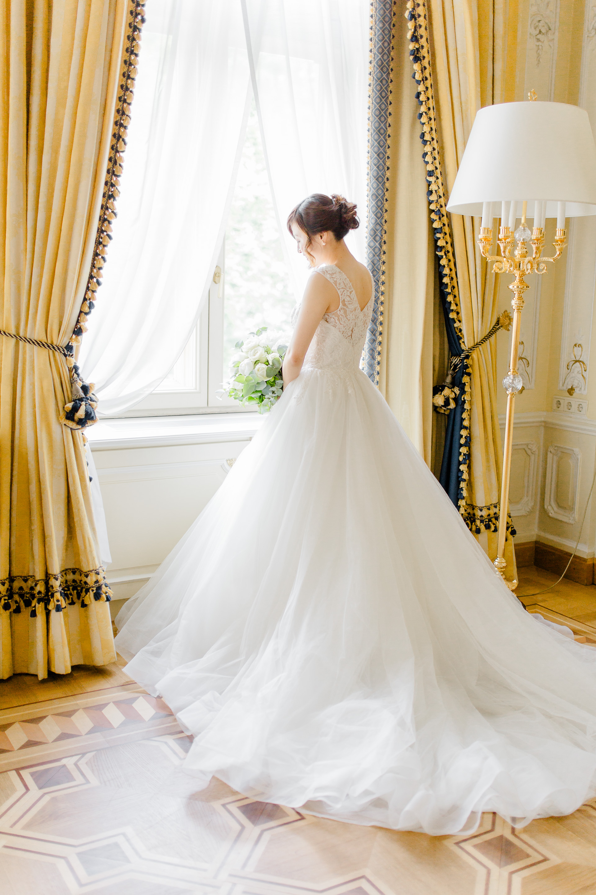 Hochzeitsfotograf Wien: Eine Braut mit Brautstrauß und Prinzessinenkleid steht am Fenster in der Fürstensuite im Hotel Imperial.