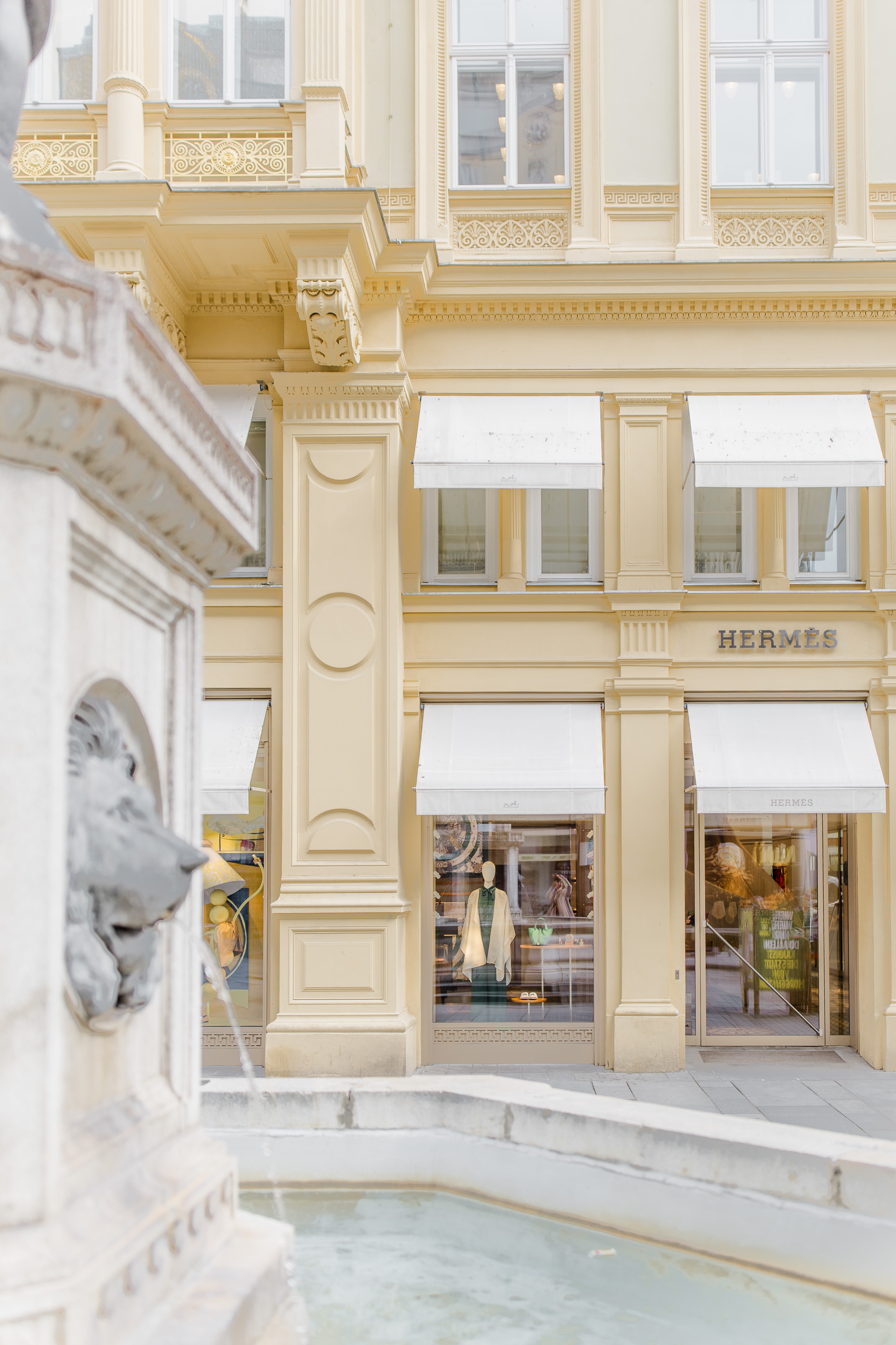 Hochzeitsfotograf Wien: Stilvolle Geschäftsfassade mit Brunnen im Vordergrund.
