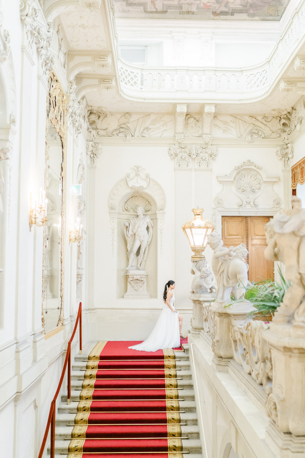Hochzeitsfotograf Wien: Eine Braut im eleganten Brautkleid schreitet eine prunkvolle Treppe im palais Kinsky herauf.