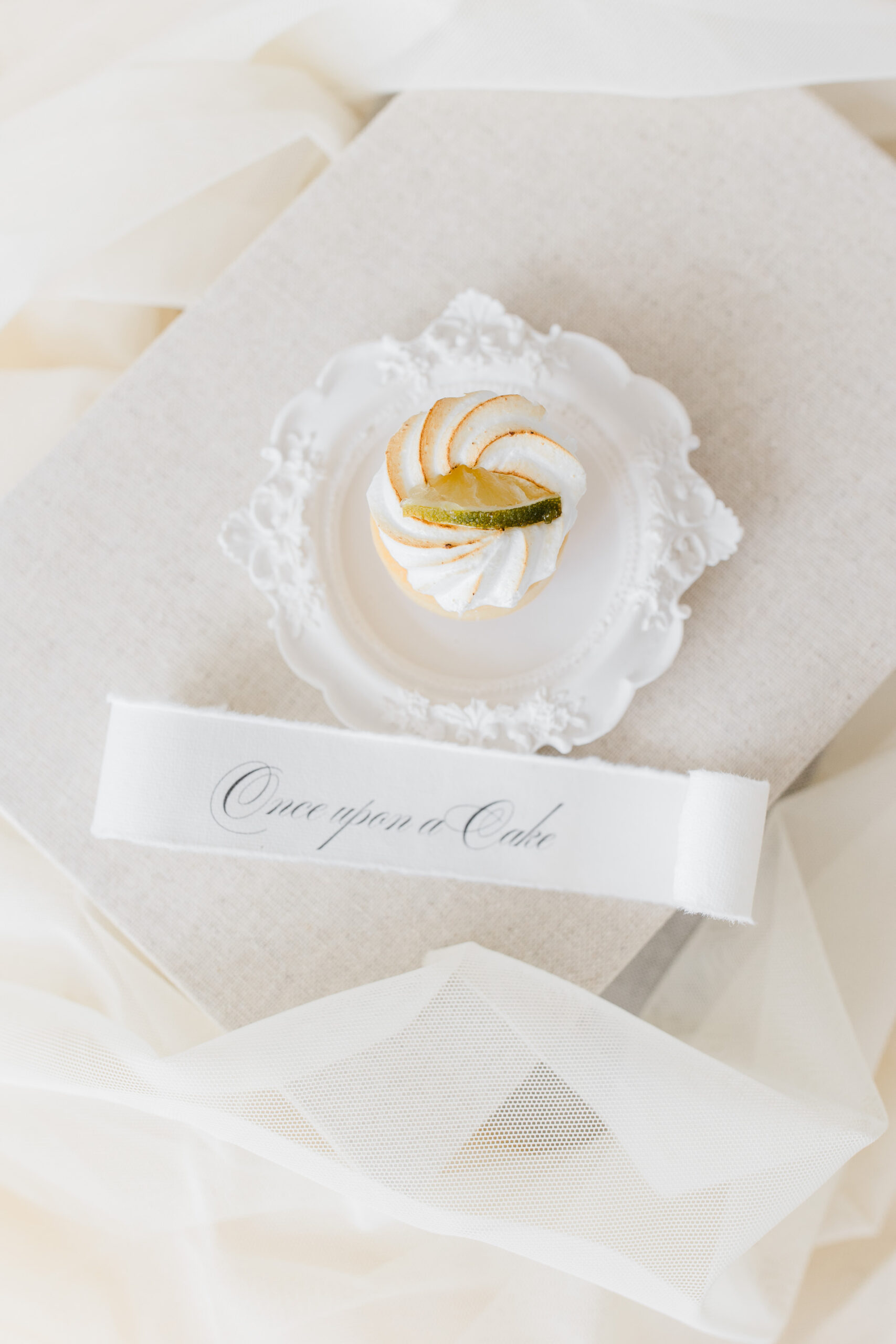 Hochzeitsfotograf Wien: elegante Aufnahme eines weißen Baisers auf einem zarten weißen Teller mit Spruchband once upon a cake.