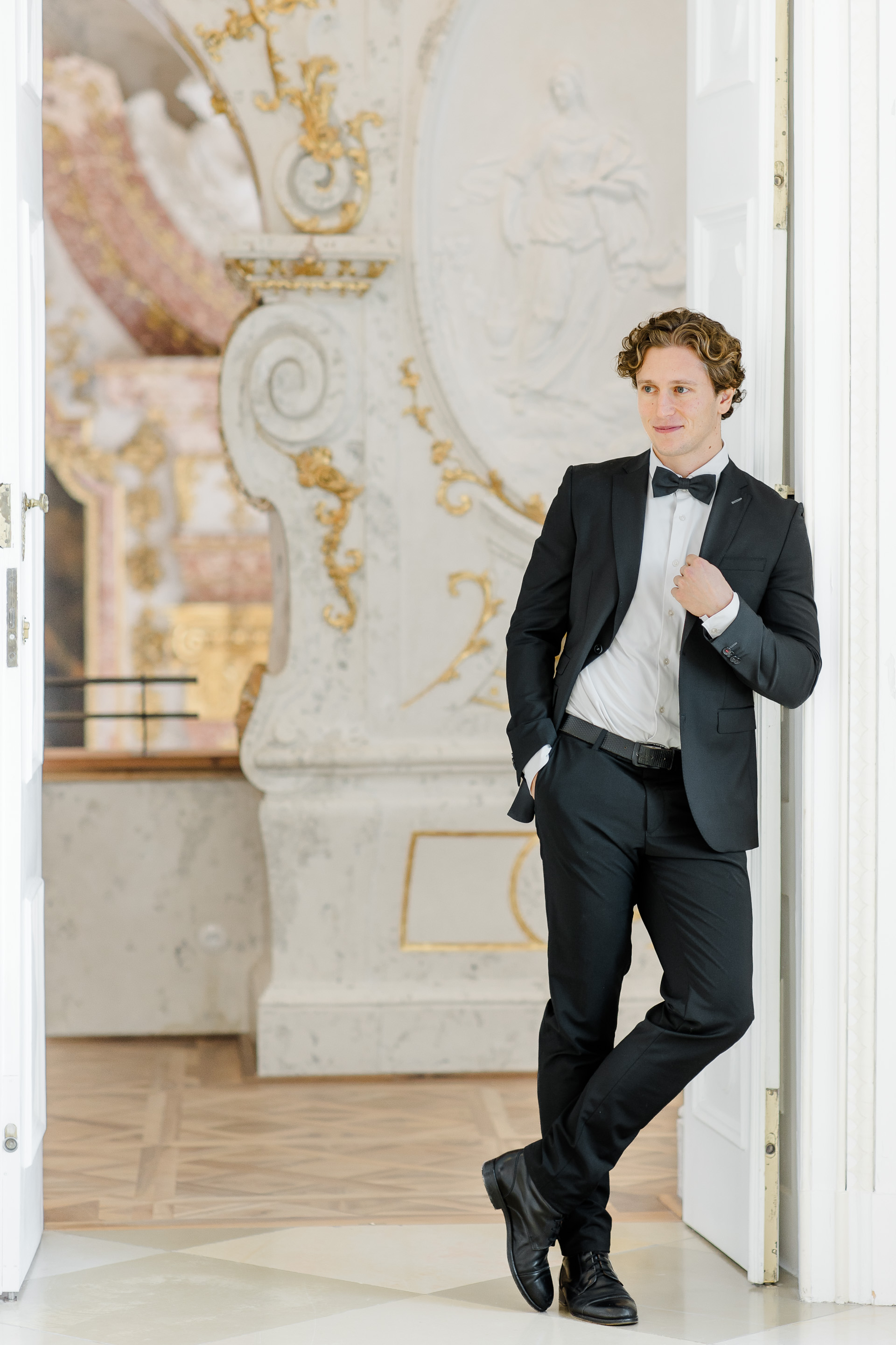 Hochzeitsfotograf Wien: Ein Bräutigam im eleganten Anzug steht an einen Türrahmen angelehnt in Schloss Hof.