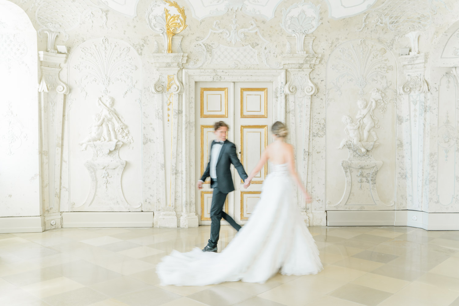 Hochzeitsfotograf Wien: Brautpaar in bewegter Unschärfe vor in einem prunkvollen Raum mit Marmor und weißem und vergoldetem Stuck.
